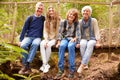 Grandparents and teens sit on bridge in forest, full length