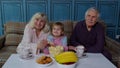 Grandparents watching cartoons movies on TV television with granddaughter at home, happy laughing Royalty Free Stock Photo