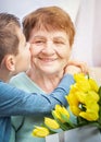 Grandson congratulates grandma on holiday. Grandmother has bunch of yellow flowers. Kindness to senior woman. Royalty Free Stock Photo