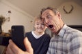 Grandson With Grandfather Pulling Faces And Taking Selfie On Mobile Phone At Home Royalty Free Stock Photo