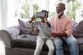 Grandson with grandfather using virtual reality headset in living room