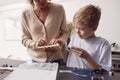 Grandson With Grandmother Assembling Electronic Components To Build Robot Together At Home