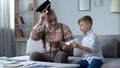 Grandson playing with toy airplane, grandfather in cap saluting to little pilot Royalty Free Stock Photo