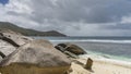 Granite boulders are piled on a sandy beach at the water\'s edge.