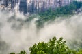 A granite mountain with high cliffs and low lying clouds.