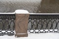 A granite pillar of a metal fence on the Shluzovaya embankment of the Drainage channel is covered with snow, water surface,