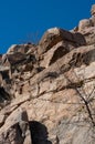 Granite rocks close-up on background blue sky with white clouds, green leaves on treetops. Royalty Free Stock Photo