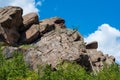 Granite rocks close-up on background blue sky with white clouds, green leaves on treetops. Royalty Free Stock Photo