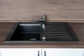 Granite sink with a shiny chrome faucet in a brand new kitchen with dark brown wood