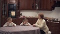 Granny and two lovely granddaughters sitting in large kitcken at the table eatting soup. Happy family have lunch at home