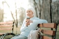 Septuagenarian granny taking pleasure of coffee on the park seat.