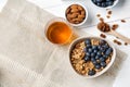 Granola with blueberries in bowl, almonds and honey on white table