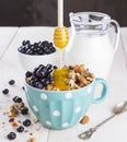 Granola with blueberry, mint, honey and milk in blue bowl with milk jug on a white table and metal spoon Royalty Free Stock Photo