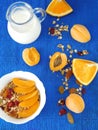 Granola with dried berries in a white bowl surrounded by apricots, oranges and a jug of milk