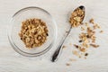 Granola in glass bowl, muesli in spoon, scattered granola on table. Top view