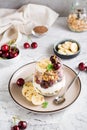 Granola with Greek yogurt, cherry and banana in a glass on the table. Vertical view