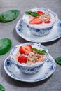 Granola, muesli with strawberries and yogurt decorate with mint in a ceramic bowls on wood grey background.