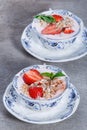 Granola, muesli with strawberries and yogurt decorate with mint in a ceramic bowls on wood grey background