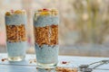 Granola pudding in two glasses with chia, fresh sliced banana and pomegranate seeds on the white wooden table. Exquisite dessert