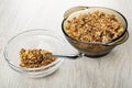 Granola, spoon in transparent bowl, brown bowl with muesli on table