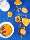 Granola in a white bowl surrounded by apricots and oranges