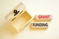 Grant funding symbol. Concept words Grant funding on wooden blocks. Beautiful white table white background. Wooden empthy chest.