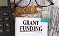 GRANT FUNDING - words on a white piece of paper on the background of a calculator, pennies and glasses Royalty Free Stock Photo