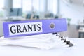 Grants, the term is written on a folder of documents in trendy purple, lying on a stack of documents on an office table against Royalty Free Stock Photo