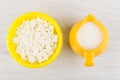 Granular fatless cottage cheese in yellow bowl, jug with yogurt Royalty Free Stock Photo