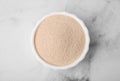 Granulated yeast in bowl on white marble table, top view