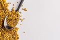 Granules of bee pollen on a sheet of white paper with a teaspoonful of granules Royalty Free Stock Photo