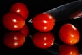 Grape tomatoes against a black background being sliced with a sharp knife on a highly reflective surface.  Vibrant colors Royalty Free Stock Photo