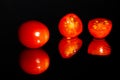 Grape tomatoes against a black background being sliced with a sharp knife on a highly reflective surface. Vibrant colors. Royalty Free Stock Photo