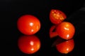Grape tomatoes against a black background being sliced with a sharp knife on a highly reflective surface. Vibrant colors. Royalty Free Stock Photo