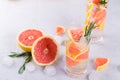 Grapefruit lemonade. Two glasses of refreshing drink, water with grapefruit, rosemary branches and ice. Recipe concept,