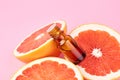 Grapefruit pure essential oil with fresh grapefruit halves on pink background. Beauty and health care concept