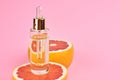 Grapefruit pure essential oil with fresh grapefruit halves on pink background