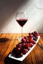 Grapes and wine. Closeup of a platter of grapes with a glasse of red wine in the background. Rustic white wall