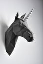 Graphitic black coloured paper unicorn`s head hanging on white wall.