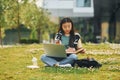 On the grass with laptop on legs. Young asian woman is outdoors at daytime