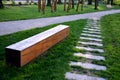 Bench one piece of wood made prism park painted brown footsteps concrete rectangles gray in the lawn and trees Royalty Free Stock Photo