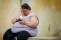 Grasse, France - August 6, 2011: overweight woman reading a phone sitting on a stone bench