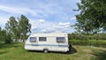 On the grassy bank of the river stands a caravan trailer for a comfortable fishing vacation. There are trees nearby and there is a