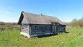 On a grassy lawn stands an old wooden house with boarded-up windows and a slate roof. Next to it are trees and shrubs. Behind the Royalty Free Stock Photo