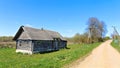 On a grassy lawn stands an old wooden house with a slate roof. Nearby there are trees and bushes. Behind the house is an agricultu Royalty Free Stock Photo