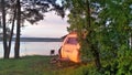 The grassy shore of the lake, the trees growing on it and the caravan trailer standing near the water are illuminated by the rays Royalty Free Stock Photo