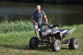 On the grassy shore near the water is a quad parked and a man stands next to the quad
