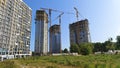 On a grassy urban area, high-rise residential buildings are being built with cranes. Nearby, trees are growing and various constru Royalty Free Stock Photo