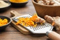 Grated fresh turmeric roots and grater. Bowls of whole and grated curcuma roots, turmeric powder on background.