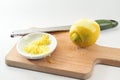 Grated lemon zest in a small bowl, fruit and grater on a wooden kitchen board, light background, copy space